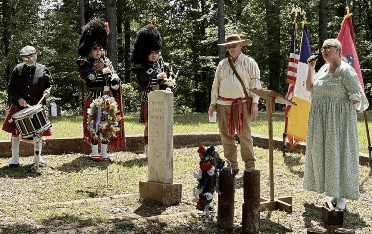 Outdoor memorial ceremony with bagpipers and flags